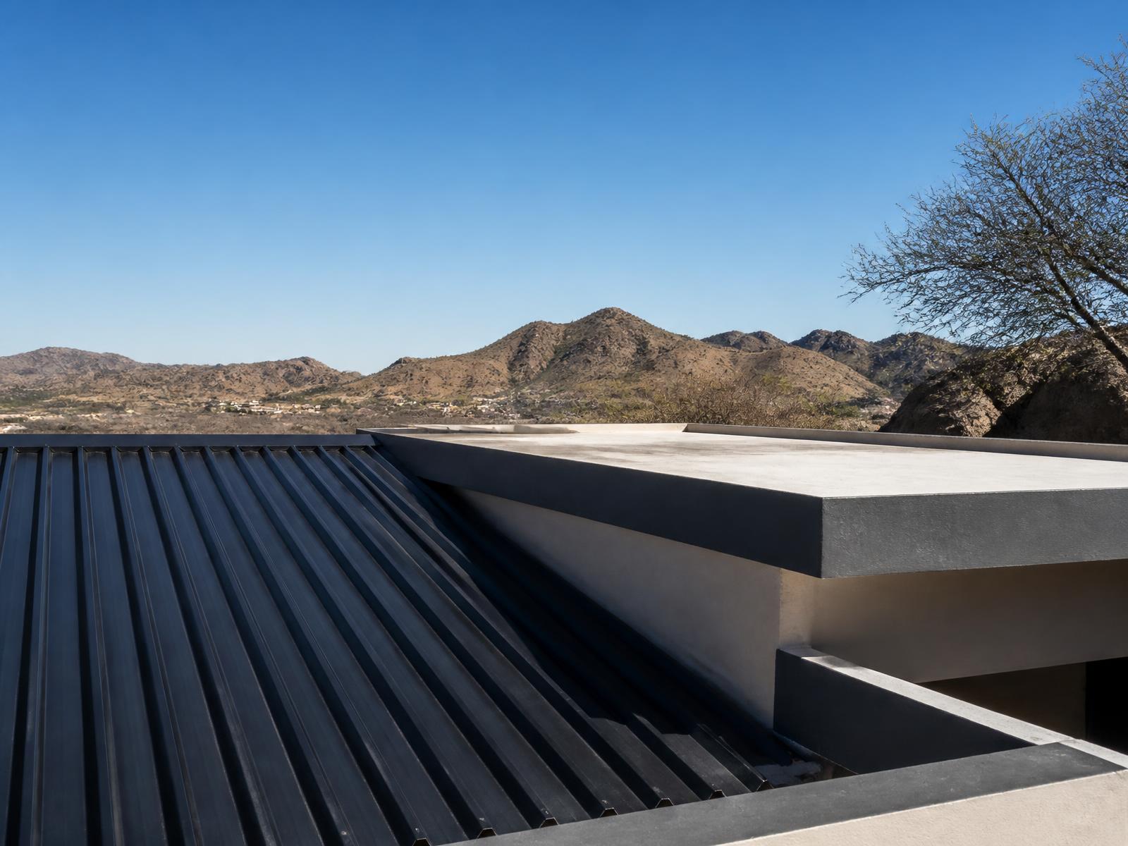 Charcoal metal sheeting meeting a flat concrete parapet roof against the hills above Windhoek